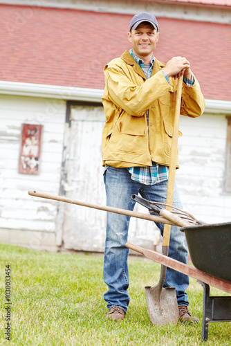 Outdoor, shovel and happy man in portrait with wheelbarrow, farming and agriculture with pride by shed. Countryside, male person and farmer with equipment for transport, cleaning and spade as tools photo