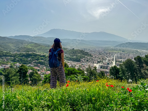 Tourist woman on colorful spring meadow overlooking idyllic town Berat seen from hilltop castle, Albania. Tranquil valles durrounded by majestic mountain Tomorr and rolling lush green hills. Tourism photo