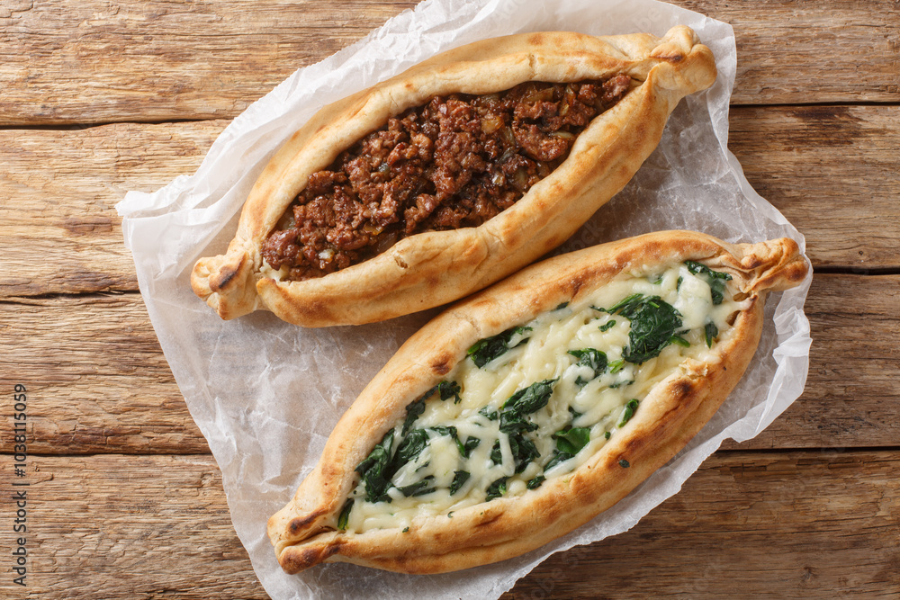 Traditional turkish baked dish pide with ground meat, cheese, spinach and spicy close-up on wooden board on table. Horizontal top view from above