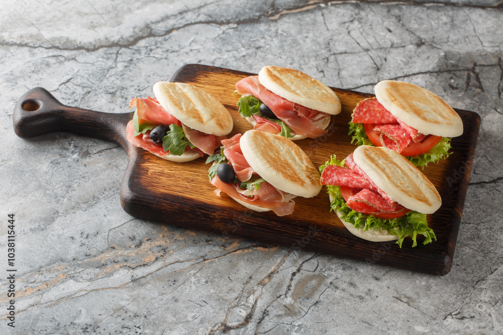 Italian tigelle or Crescentina modenese with sausage, jamon and fresh vegetables close-up on a wooden board on the table. Horizontal