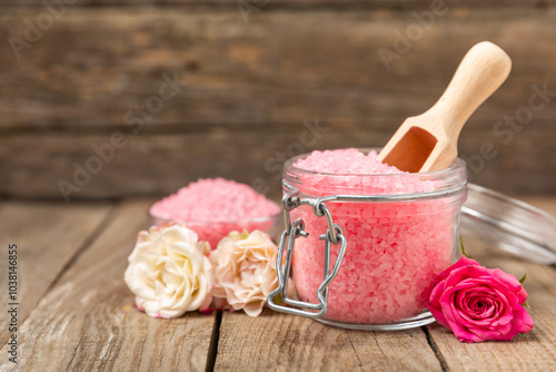 Sea salt for bath with aroma and rose flowers on textured wooden background. Pink sea salt. Spa treatments. Natural salt with herbs and essential oils. skincare concept. Meso for text. Copy space photo