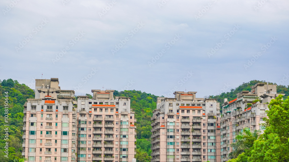 A top view of a residential area in Taipei, Taiwan that full of apartment buildings that are surrounded with trees and mountain. A symbol of good life, balance between city and nature A top view of a residential area in Taipei, Taiwan that full of apartment buildings that are surrounded with trees and mountain. A symbol of good life, balance between city and nature
