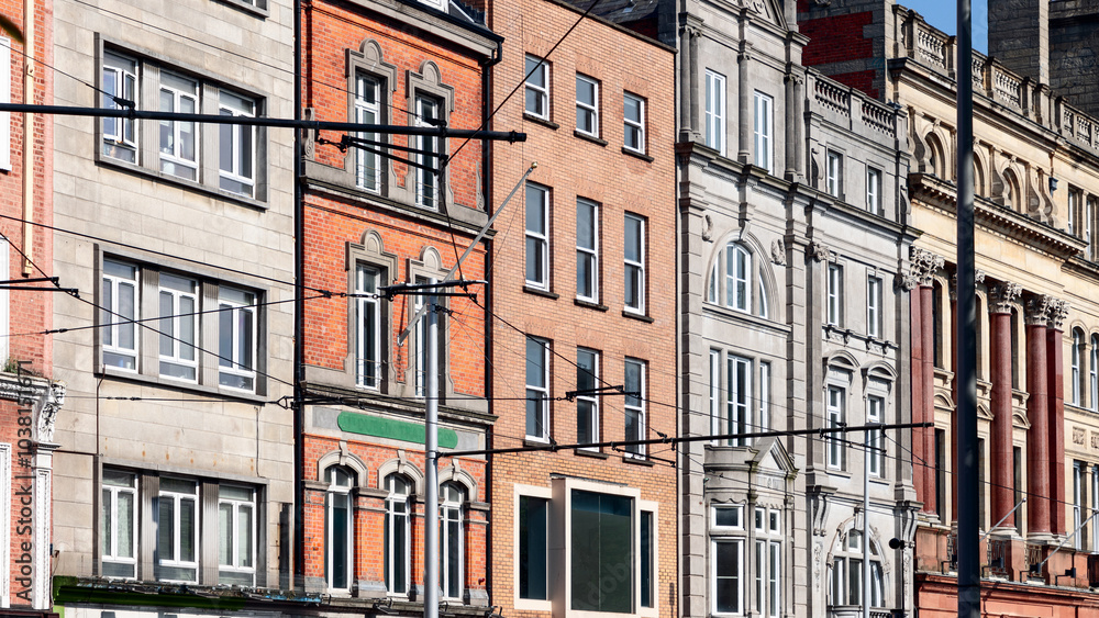 Fototapeta premium Facades of various buildings in Dublin, showcasing a contrast of red brick and stone architecture. The image highlights the urban character of the city, with the tram lines crossing in front