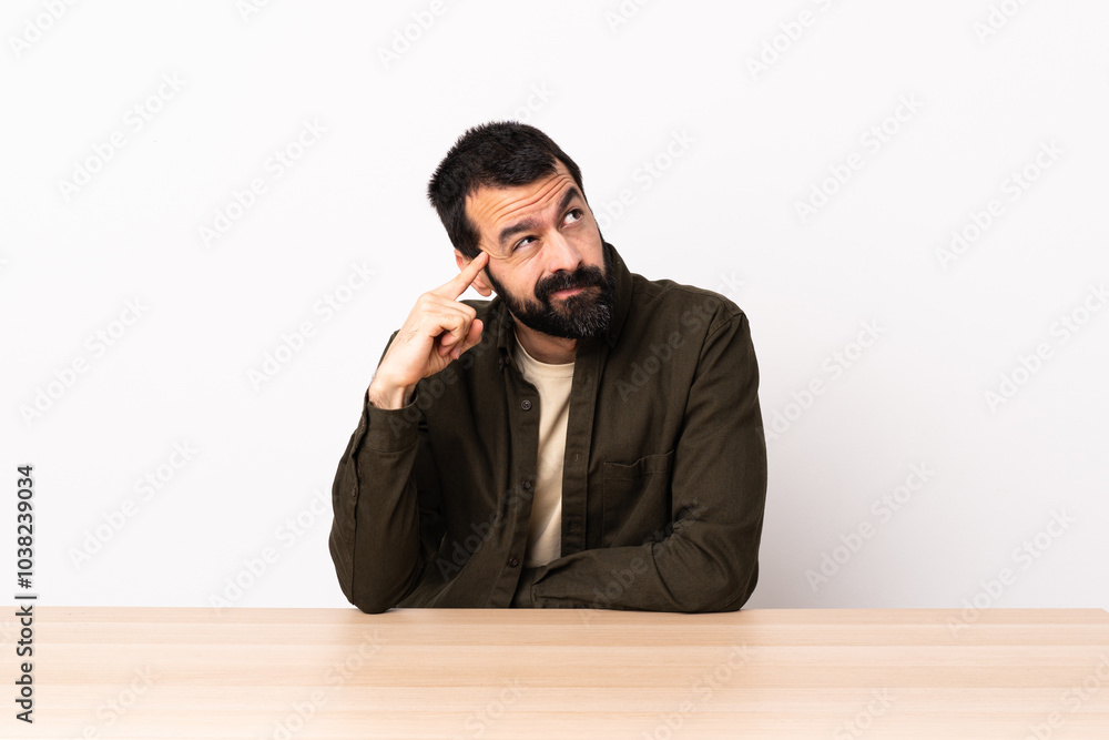 Caucasian man with beard in a table making the gesture of madness putting finger on the head. Caucasian man with beard in a table making the gesture of madness putting finger on the head.