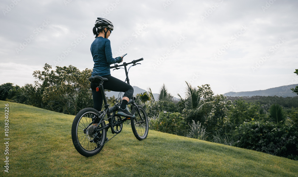 Woman cyclist using a smartphone on tropical mountain peak Woman cyclist using a smartphone on tropical mountain peak