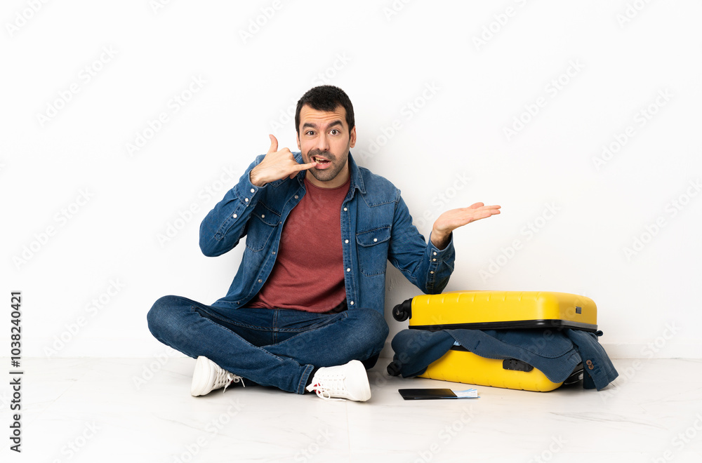 Caucasian handsome man with a suitcase full of clothes sitting on the floor at indoors making phone gesture and doubting Caucasian handsome man with a suitcase full of clothes sitting on the floor at indoors making phone gesture and doubting