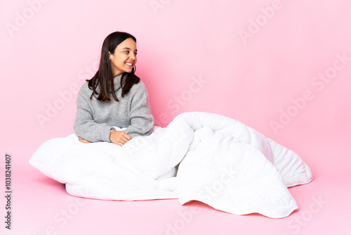 Young mixed race woman wearing pijama sitting on the floor looking to the side and smiling photo