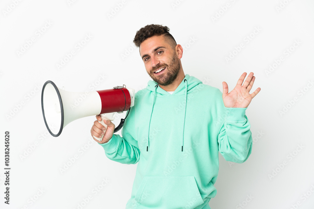 Caucasian man isolated on white background holding a megaphone and saluting with hand with happy expression