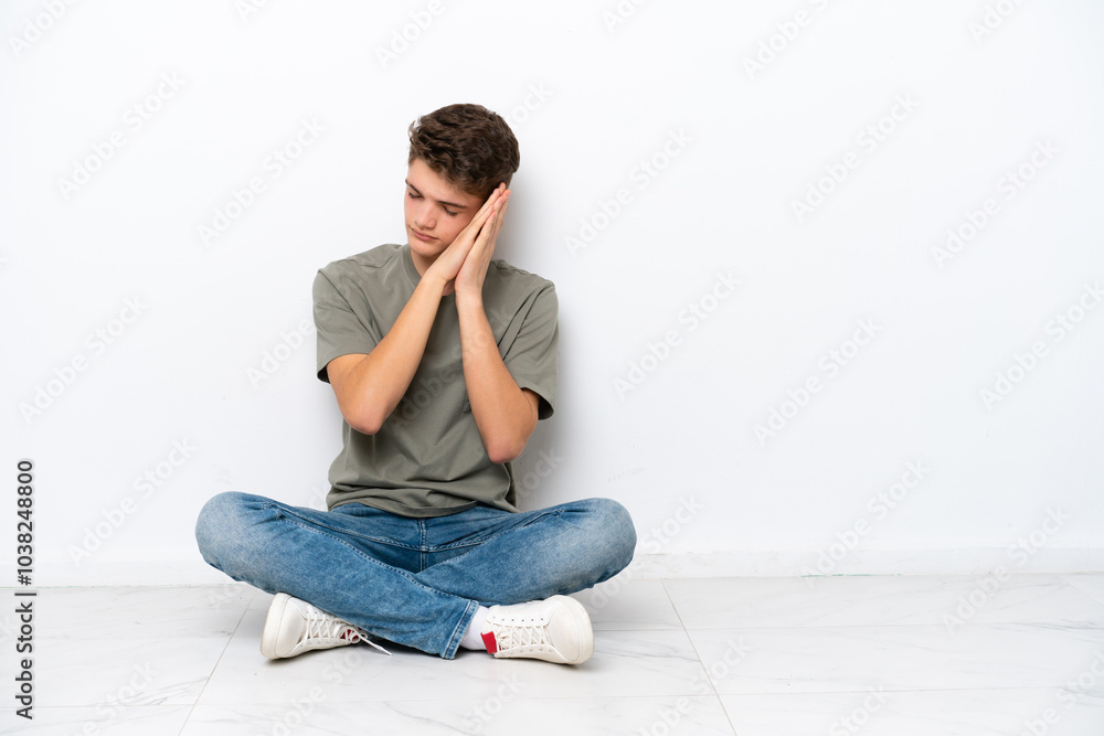 Teenager Russian man sitting on the floor isolated on white background making sleep gesture in dorable expression Teenager Russian man sitting on the floor isolated on white background making sleep gesture in dorable expression