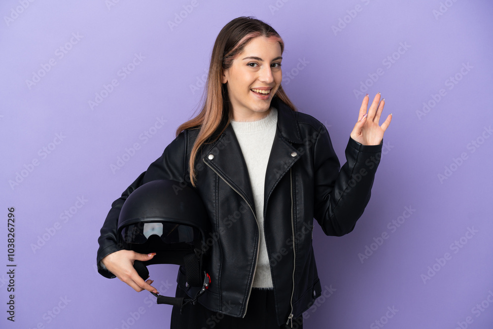Young caucasian woman holding a motorcycle helmet isolated on purple background saluting with hand with happy expression Young caucasian woman holding a motorcycle helmet isolated on purple background saluting with hand with happy expression