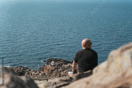 Man seated on a cliff, admiring the view and sun