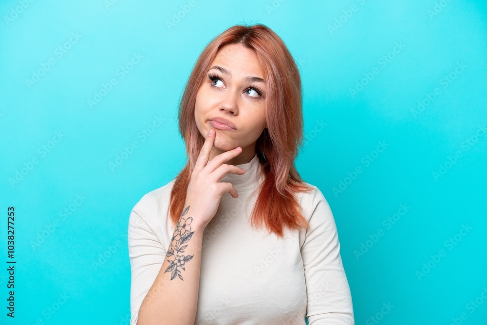 Young Russian woman isolated on blue background having doubts while looking up Young Russian woman isolated on blue background having doubts while looking up