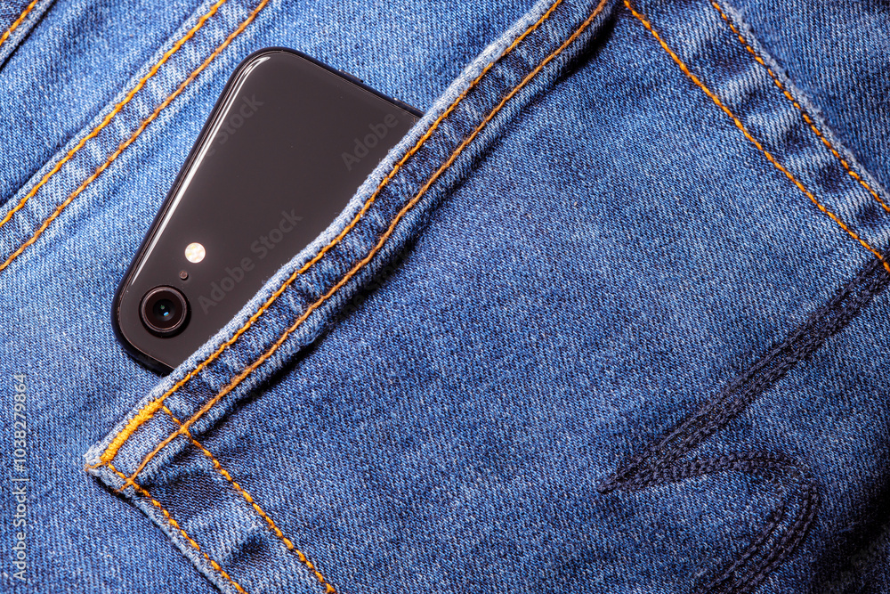 Worn denim trousers. Machine stitch close up. Denim texture in blue. The concept of repairing old clothes. Sewing factory. A smartphone is peeking out of the pocket of his jeans. Worn denim trousers. Machine stitch close up. Denim texture in blue. The concept of repairing old clothes. Sewing factory. A smartphone is peeking out of the pocket of his jeans.