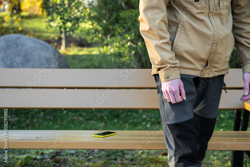 man is leaving from a bench where he lost his smartphone. Forgotten smartphone on a park bench.