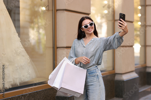 Happy woman with shopping bags taking selfie outdoors photo