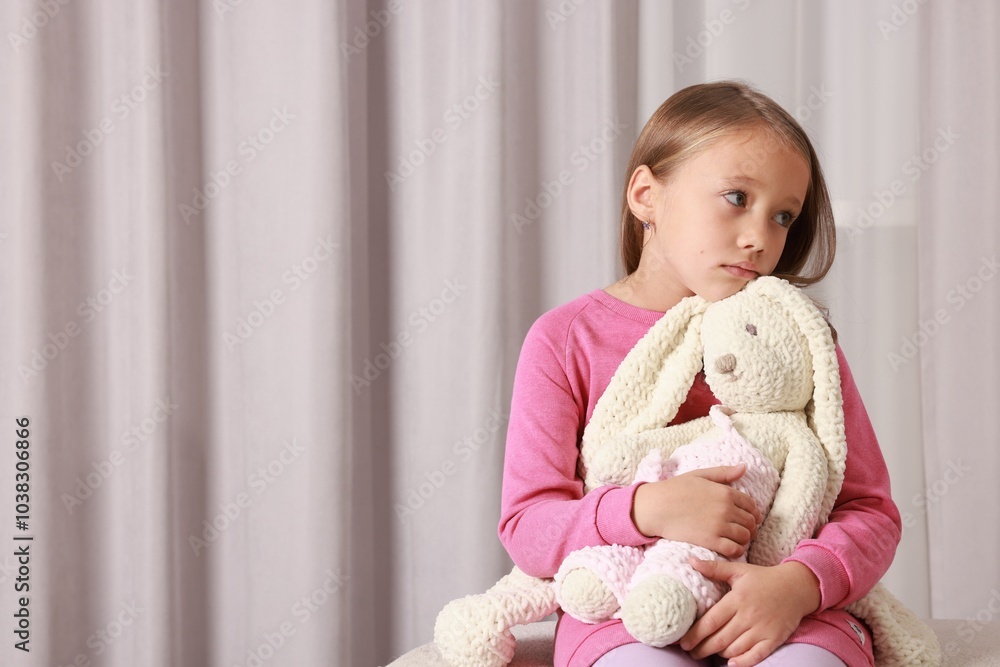 Autism concept. Lonely little girl with toy bunny on pouf at home, space for text Autism concept. Lonely little girl with toy bunny on pouf at home, space for text