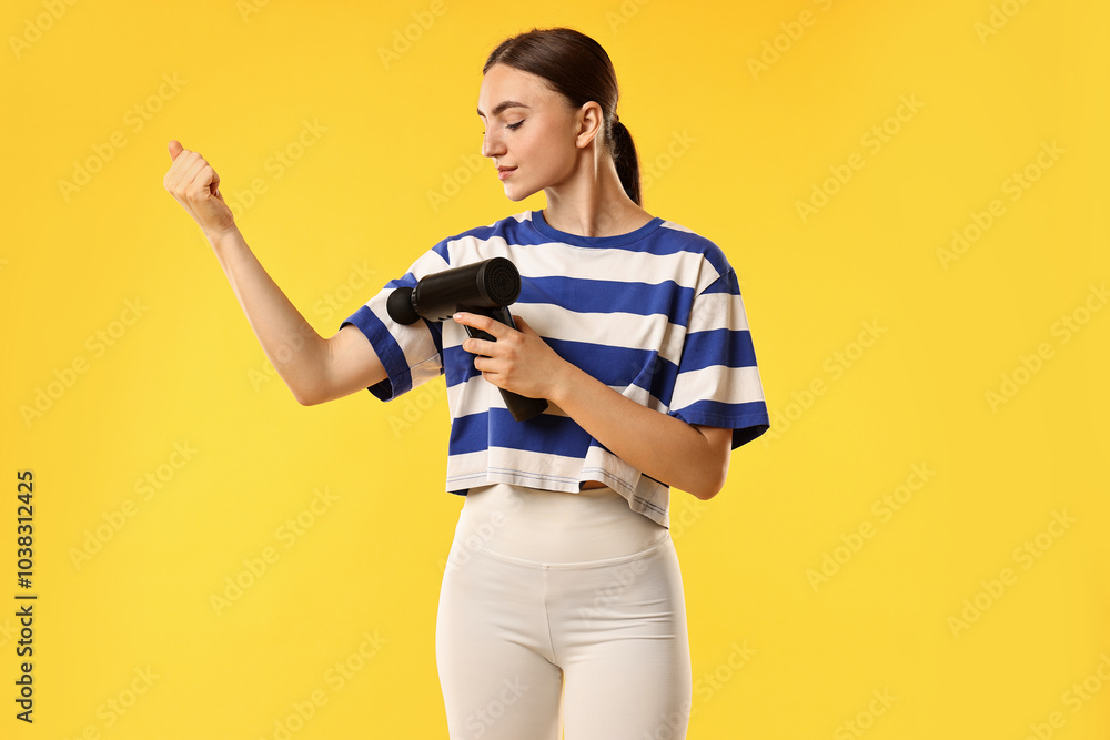 Fototapeta premium Woman using percussive massager to relieve bicep on yellow background