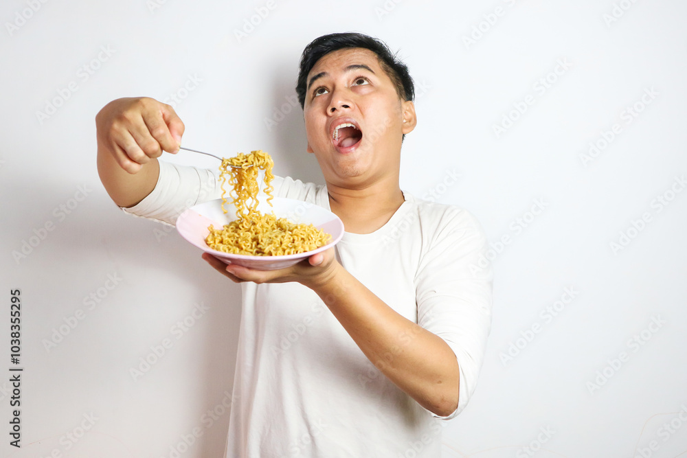 Adult Asian man showing surprised expression and looking up while eating noodles Adult Asian man showing surprised expression and looking up while eating noodles