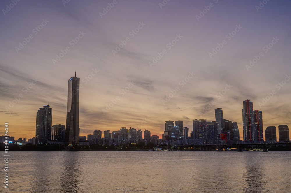 Obraz premium Sunset and silhouette view of 63 Building and high rise buildings of financial district with Wonhyo Bridge on Han River at Yeouido near Yeongdeungpo-gu, Seoul, South Korea