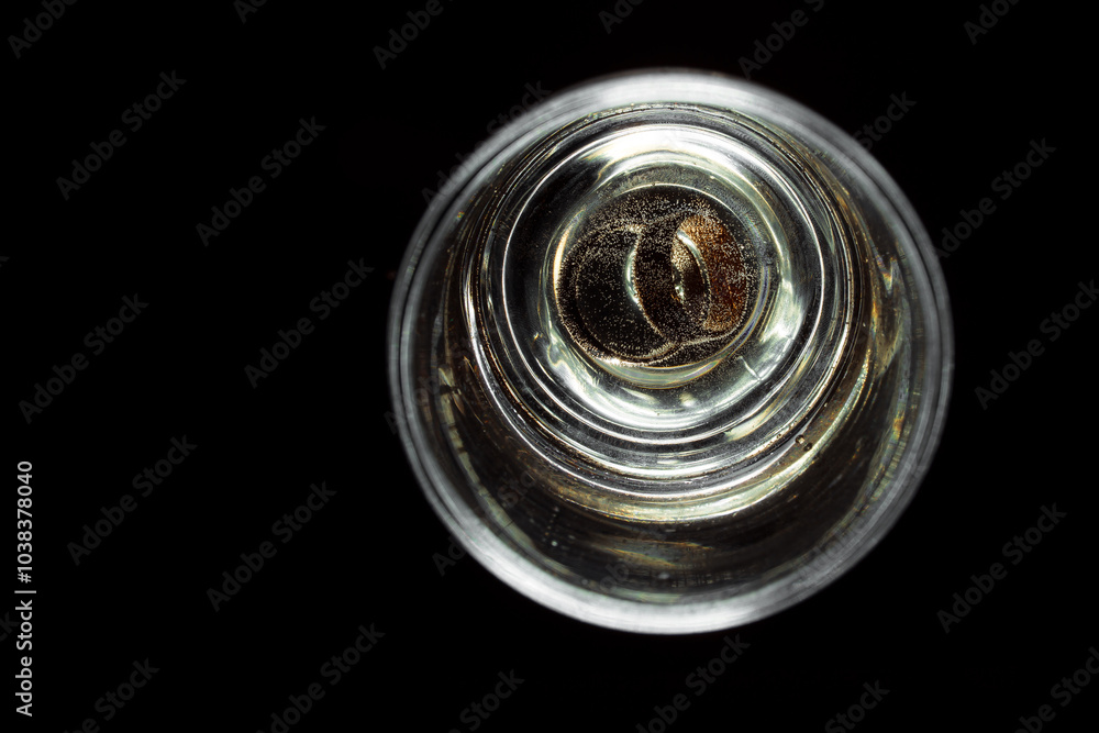 Wedding rings in a glass of champagne. Beverage gas bubbles around the jewelry. Isolate of glasses with champagne on a black background. Unique design elements for invitation, wedding cards. Wedding rings in a glass of champagne. Beverage gas bubbles around the jewelry. Isolate of glasses with champagne on a black background. Unique design elements for invitation, wedding cards.