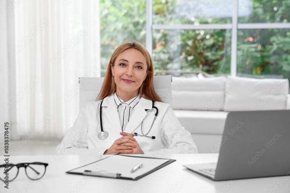 Doctor with stethoscope, laptop and clipboard at table in clinic Doctor with stethoscope, laptop and clipboard at table in clinic