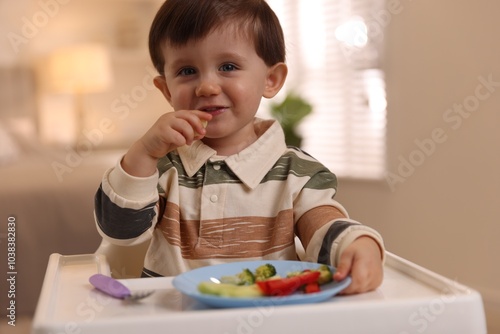 Cute little baby eating healthy food in high chair at home