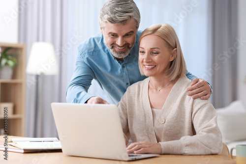 Happy middle aged couple working with laptop at table indoors