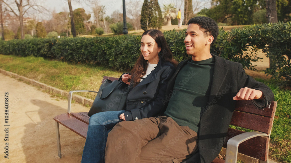 Happy couple laughing together on park bench with greenery and historic architecture in background Happy couple laughing together on park bench with greenery and historic architecture in background