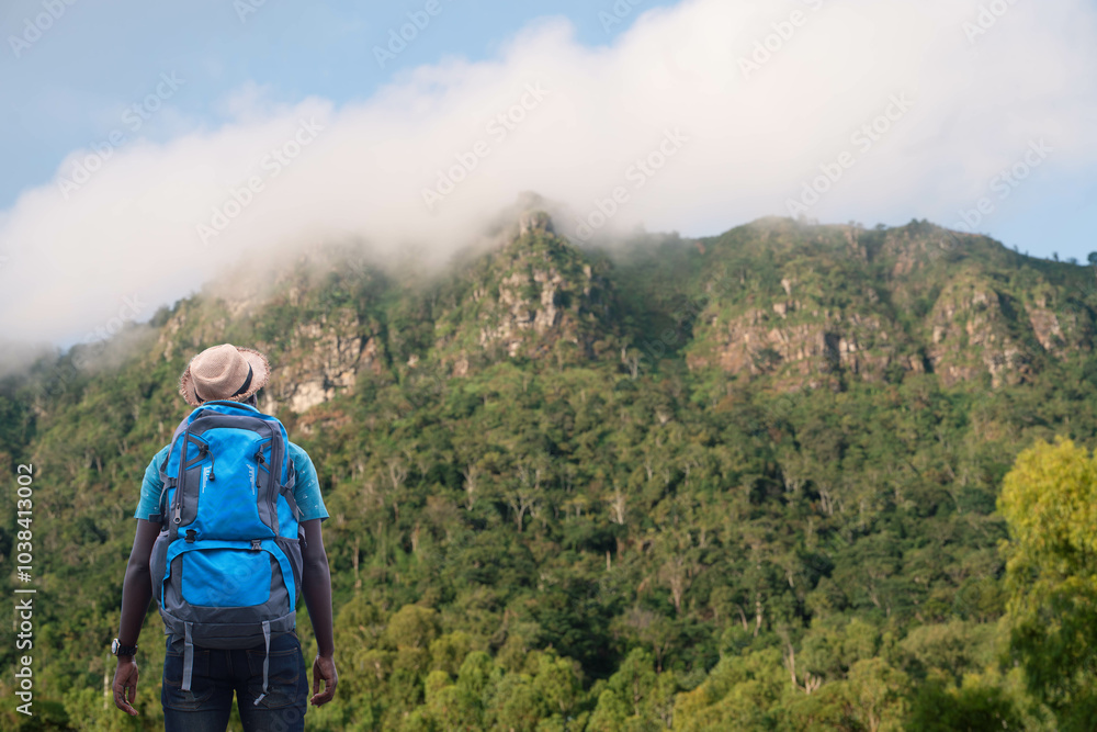 African traveler and mountain climber with backpack standing looking at foggy mountain. Adventure and nature travel concept. African traveler and mountain climber with backpack standing looking at foggy mountain. Adventure and nature travel concept.