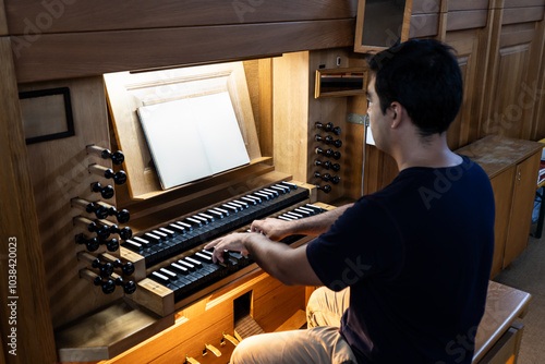 Left side view of organist sitting at organ with blank musical score playing organ in Catholic Church.