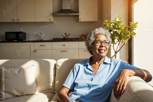 Older Black woman with curly gray hair on couch in sunlit living room photo