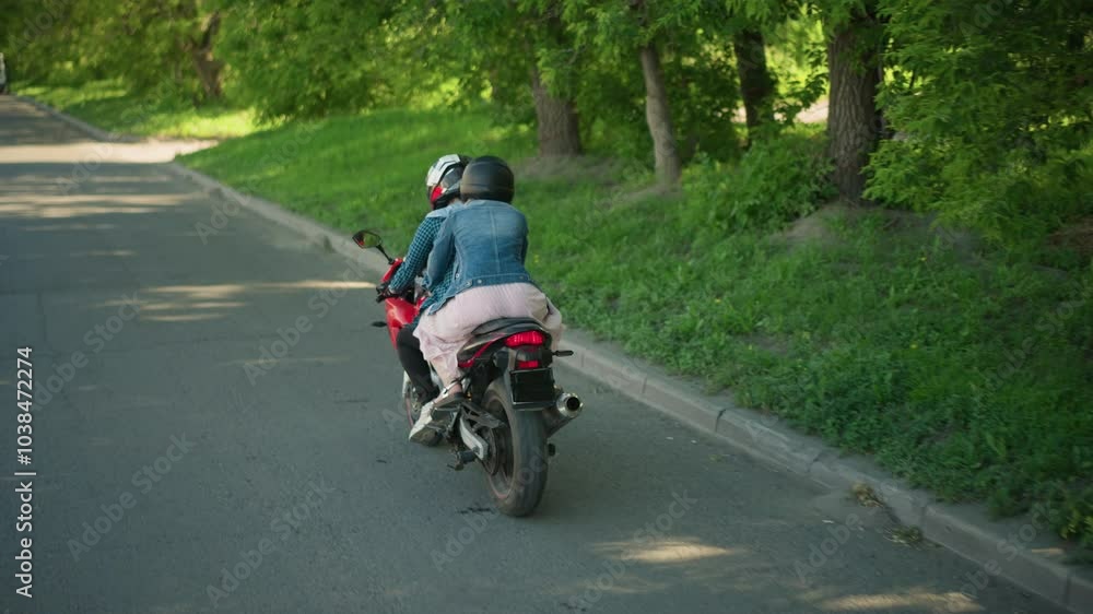 Two ladies riding a power bike on a smooth tarred road, flanked by lush green trees, the serene road stretches ahead as they travel, with a gentle curve seen in the distance on the right Two ladies riding a power bike on a smooth tarred road, flanked by lush green trees, the serene road stretches ahead as they travel, with a gentle curve seen in the distance on the right