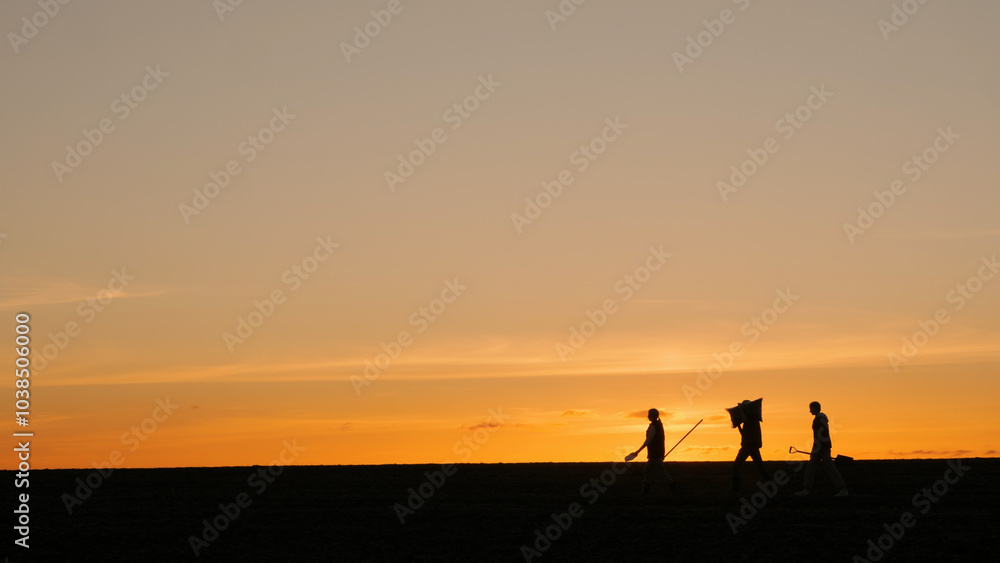 Silhouettes of three farmers in a field. Walking with equipment against the backdrop of a picturesque sunset Silhouettes of three farmers in a field. Walking with equipment against the backdrop of a picturesque sunset