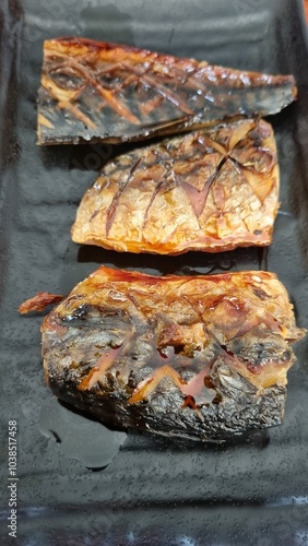 Grilled saba fish on a black plate in a Japanese restaurant