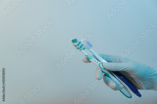 Dentist's hand in the medical glove holding two toothbrushes, dental care concept with the copy space  