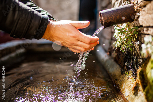 Hands collecting water from a rustic outdoor pipe