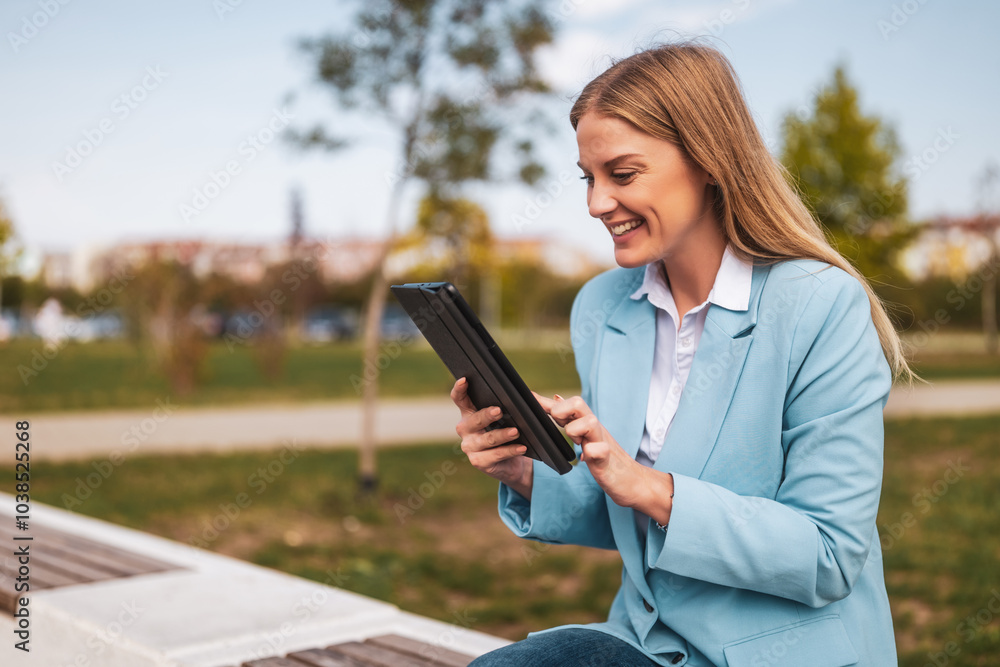 Fototapeta premium Beautiful businesswoman using digital tablet while sitting on the bench outdoor.