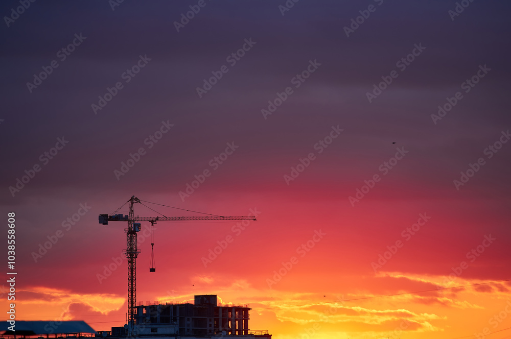 Fototapeta premium Construction Crane Silhouette Against Fiery Sunset