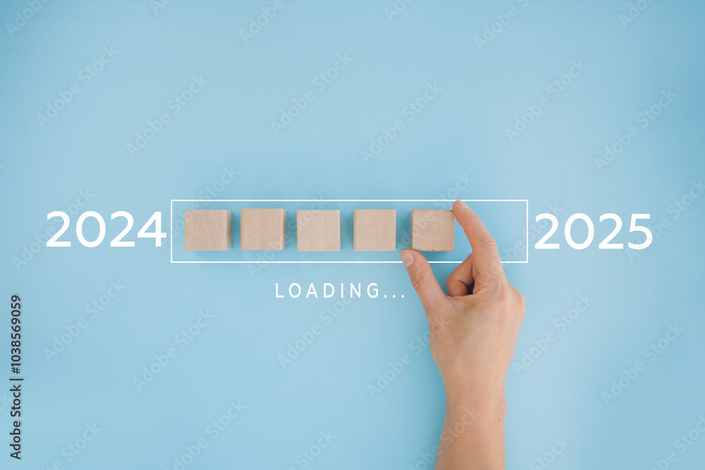 © olyphotostories - 2025 New Year Loading. Female hand moving wooden blocks with Loading bar between 2024 and 2025 on a blue background. Concept for transition, progress, new year, and future plans