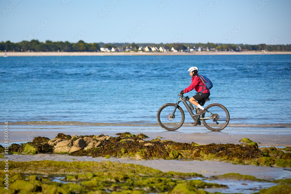 Fototapeta premium active senior woman cycling with her electric mountain bike along the beach of Loctudy, Brittany, France