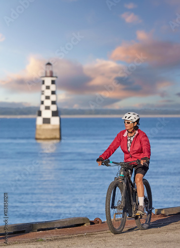 active senior woman cycling with her electric mountain bike along the beach of Loctudy in front of the black and white checkered Lighthouse, Brittany, France photo