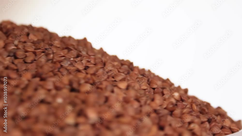 Dry Uncooked Brown Buckwheat Groats Heap on White Plate Rotating against White Background. Raw Large Buckwheat Grains. Russian, Ukrainian and Belarusian Culture Dry Uncooked Brown Buckwheat Groats Heap on White Plate Rotating against White Background. Raw Large Buckwheat Grains. Russian, Ukrainian and Belarusian Culture