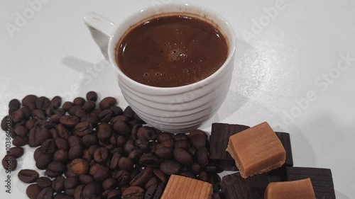 White cup with coffee, next to coffee beans and milk and chocolate toffees, slow zoom