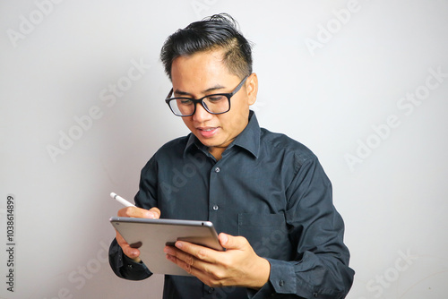 Adult Asian man smiling at the camera when working using mobile tablet gadget photo