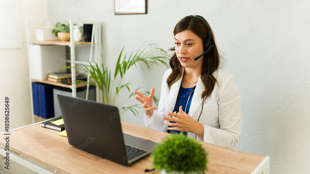 Female doctor in white coat using headset for video call with patient on laptop at clinic Female doctor in white coat using headset for video call with patient on laptop at clinic