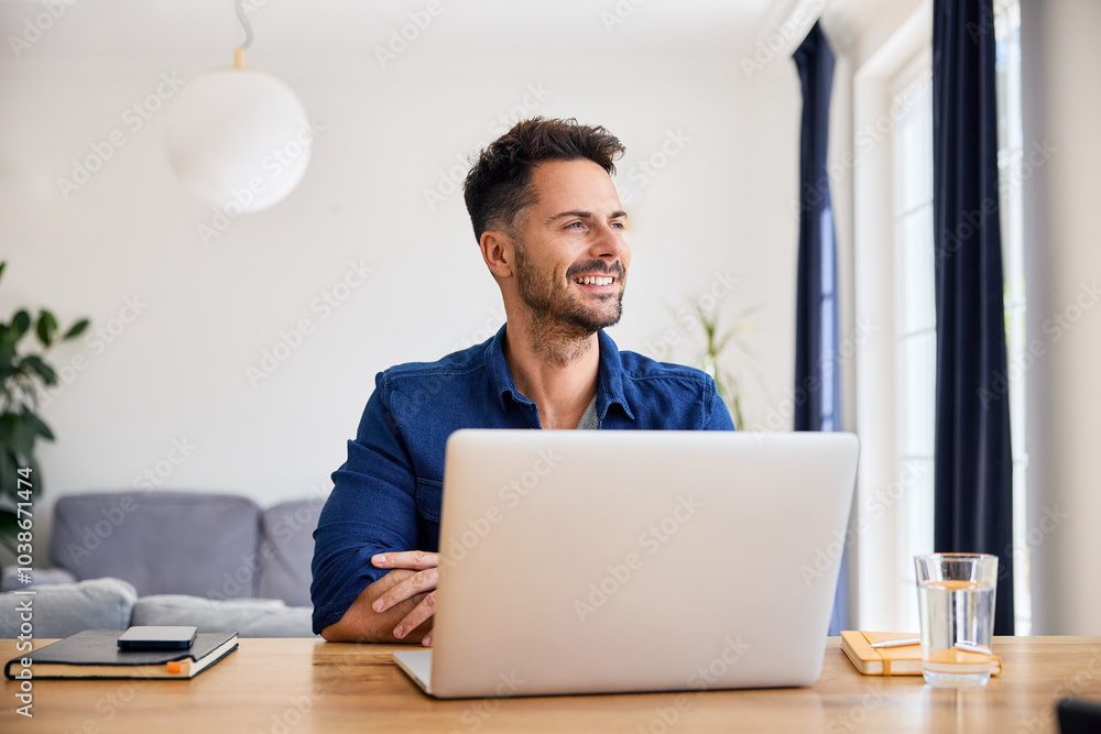 Smiling thoughtful man working on his laptop from home looking away Smiling thoughtful man working on his laptop from home looking away