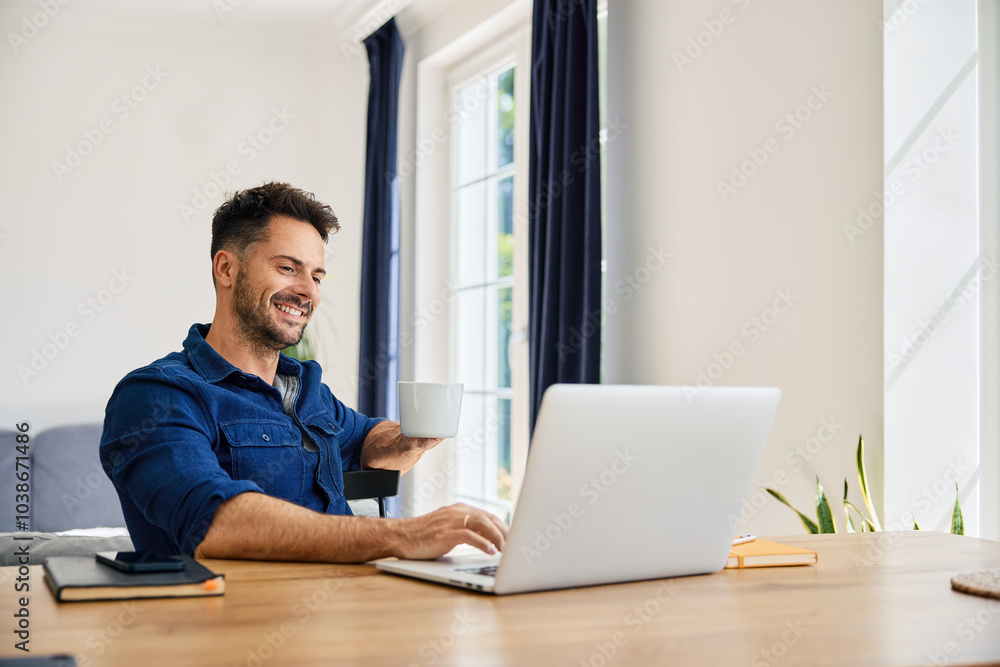 Carefree man using laptop at home sitting by a table working remotely Carefree man using laptop at home sitting by a table working remotely