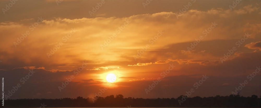 Obraz premium Stunning sunset with golden sky and dramatic clouds over a peaceful landscape