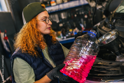 Young ginger woman mechanics pouring antifreeze. photo