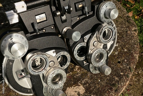 Vintage manual mechanical phoropter device, used in optometry to evaluate patient refractive errors such as myopia or hyperopia, placed on stone garden well cover, sunlit by autumn afternoon sunshine. photo